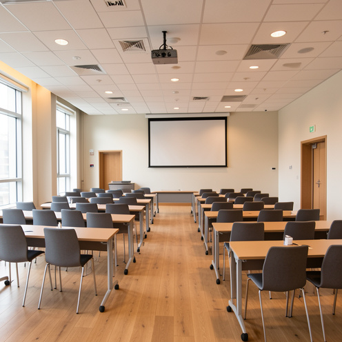 Grande salle polyvalente aménagée avec des chaises, des tables modulables, un vidéoprojecteur et un écran vierge, illustrant sa capacité et ses équipements.